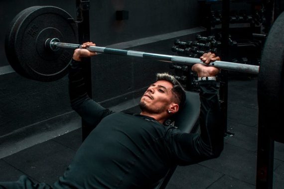 Man performing bench press with heavy barbell in a gym setting, focusing on strength training.